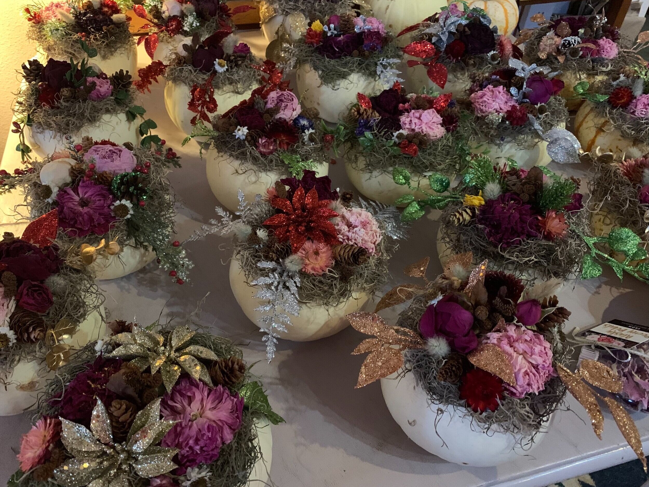 Arrangement of decorative floral centerpieces in white pumpkins, featuring a variety of dried flowers, greenery, and festive embellishments. Perfect for autumn decor and seasonal celebrations.
